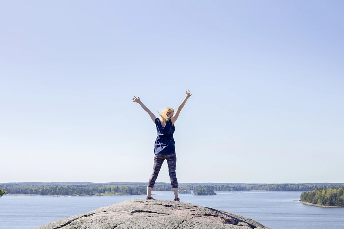 Studio Aina, Helsinki – palvelut. Nainen kukkulan alella tuulettaa kädet ilmassa.
